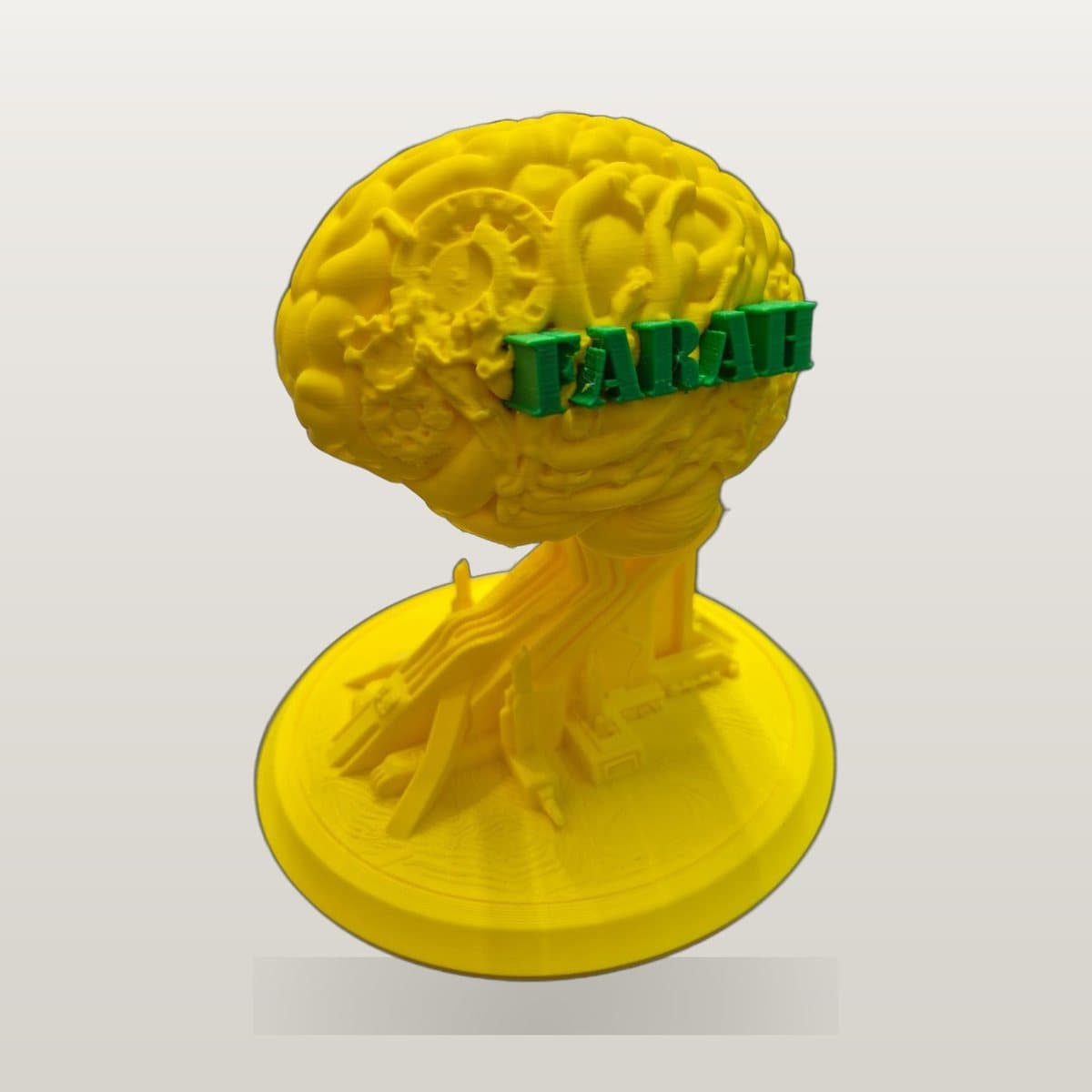 Yellow 3D printed brain model on a round base, with the name FARAH across it in green