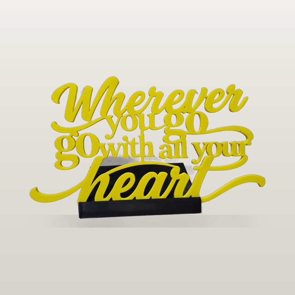 Yellow 3D printed script lettering reading 'Wherever you go, go with all your heart' on a black stand